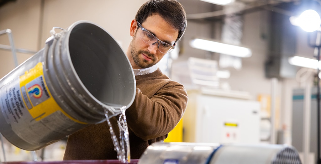 Marton Kardos pours a clear liquid from a gray bucket at the Center for Renewable Carbon.