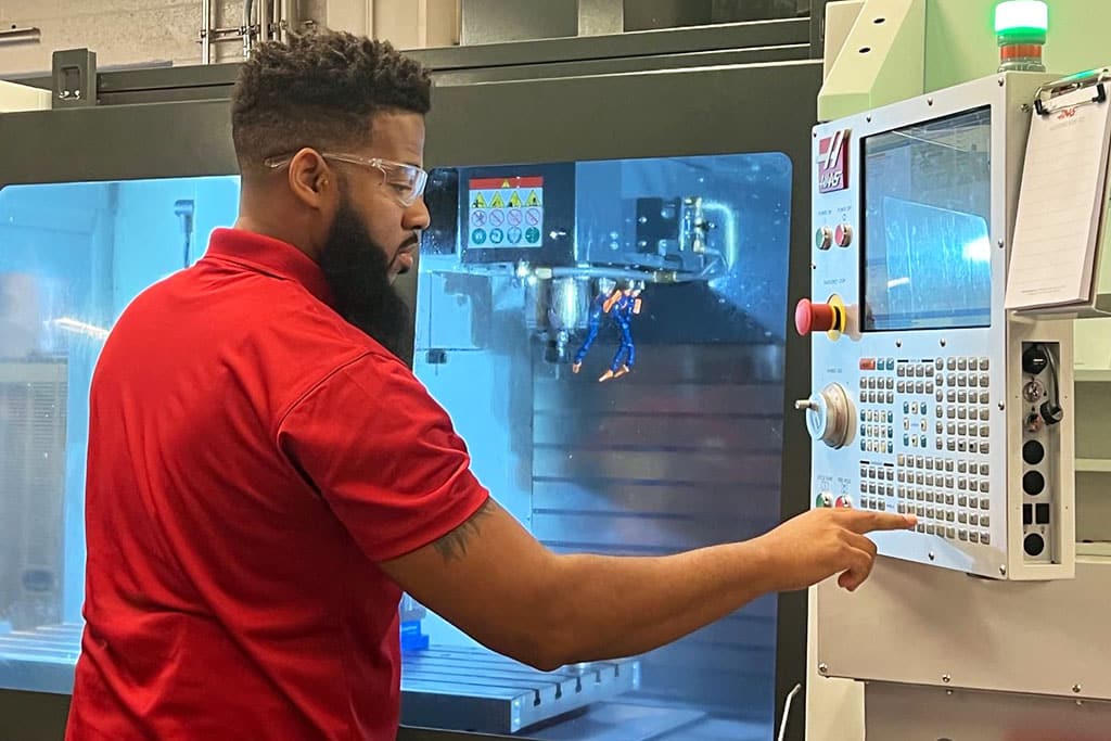 An ACE bootcamp student wearing a red polo shirt operates a machine.