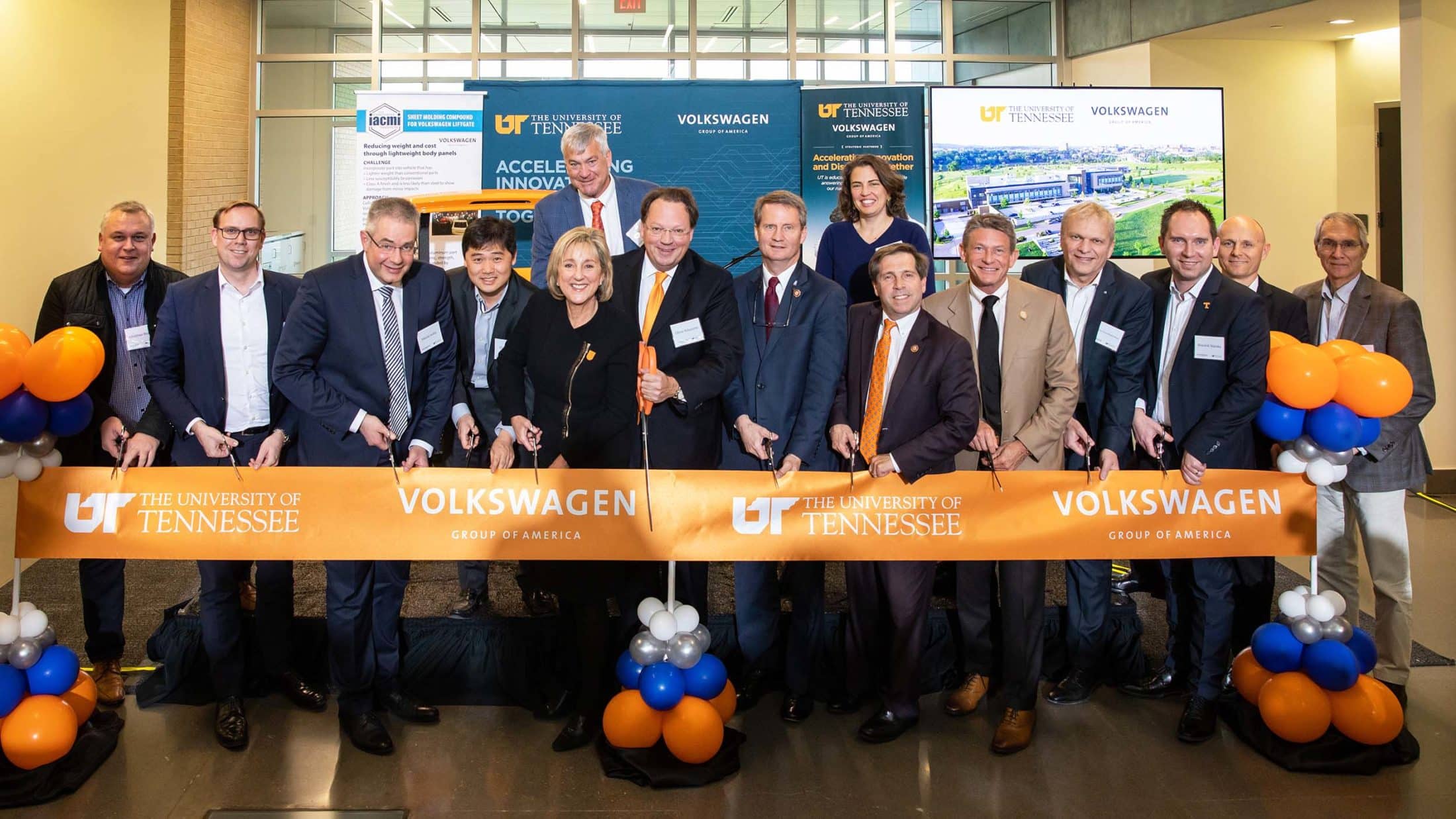 Several leaders from UT and Volkswagen prepare to cut a large orange ribbon at the announcement of the new Volkswagen Innovation Hub at UT Research Park.