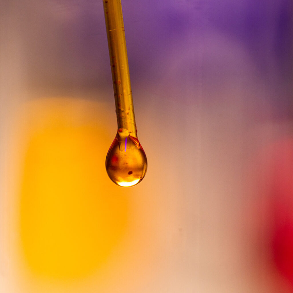A golden drop of liquid dangles at the end of a syringe inside a clear test tube.