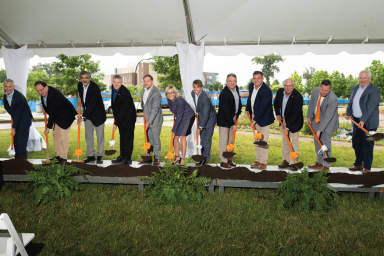 A group of people hold orange shovels with soil at the Innovation South groundbreaking.