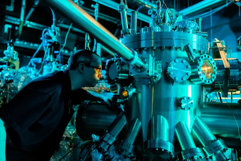 A man wearing glasses looks into a glass section of large equipment in a quantum laboratory.