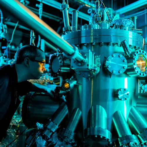 A man wearing glasses looks into a glass section of large equipment in a quantum laboratory.