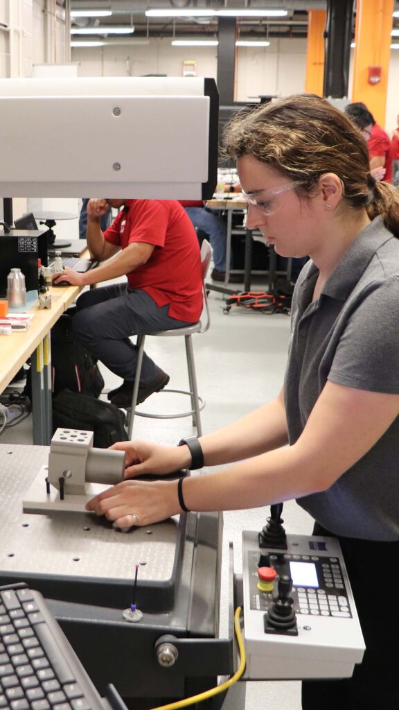 Woman wearing safety glasses and a gray polo shirt operates a machine at an ACE Training session.
