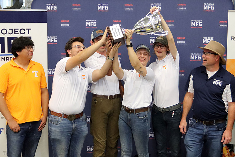 Several UT team members hold a championship trophy in the air.