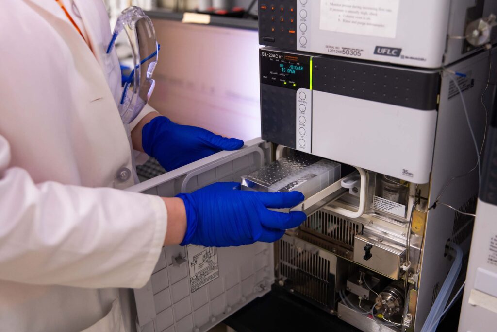 Close up of Carrie Sanford's hands as they insert a sample into a machine for high-performance liquid chromatography.