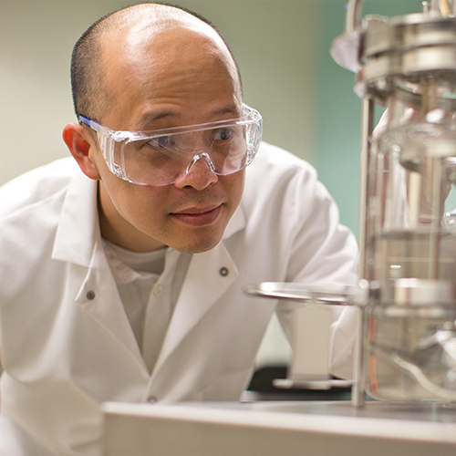 Cong Trinh in safety goggles looks closely at equipment in a lab.