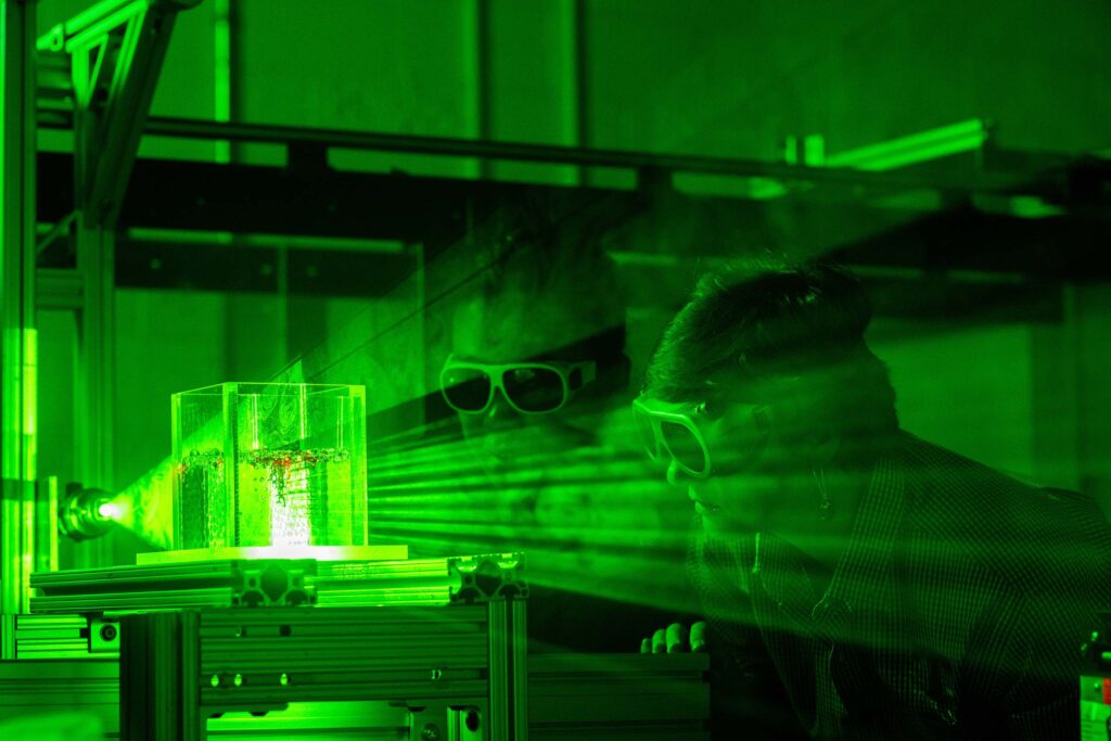 Anna Herring and Haochen Li watch as dye disperses throughout a cylinder full of clear beads.