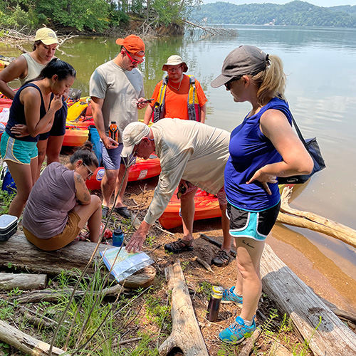 A group of interns on the banks of the Tennessee River listen as a researcher points to a map.