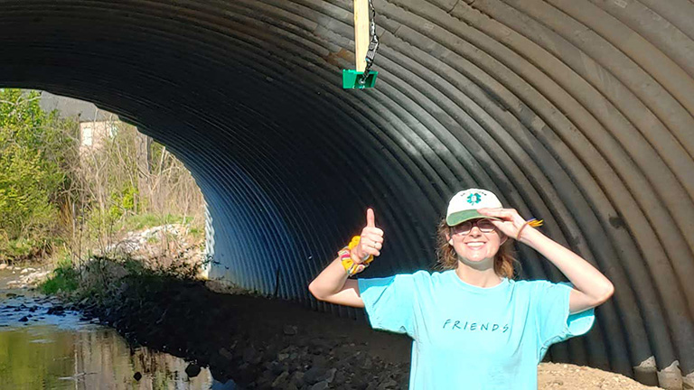 A student gives a thumbs up as she's checking a gauge in the field.