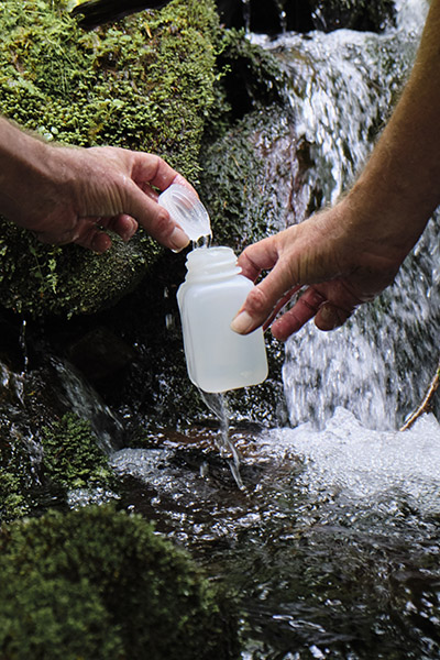 John Schwartz holds a water bottle in front of a waterfall.