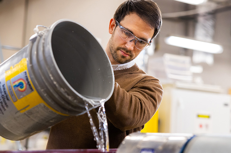 Marton Kardos pours water from a gray bucket into equipment at the Center for Renewable Carbon.