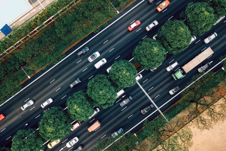 Overhead view of a multilane boulevard lined with trees and moderate traffic.