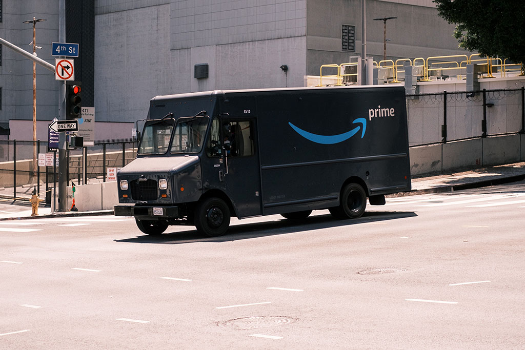 A dark blue Amazon truck drives down an urban street; photo by Andrew Stickelman on Unsplash.