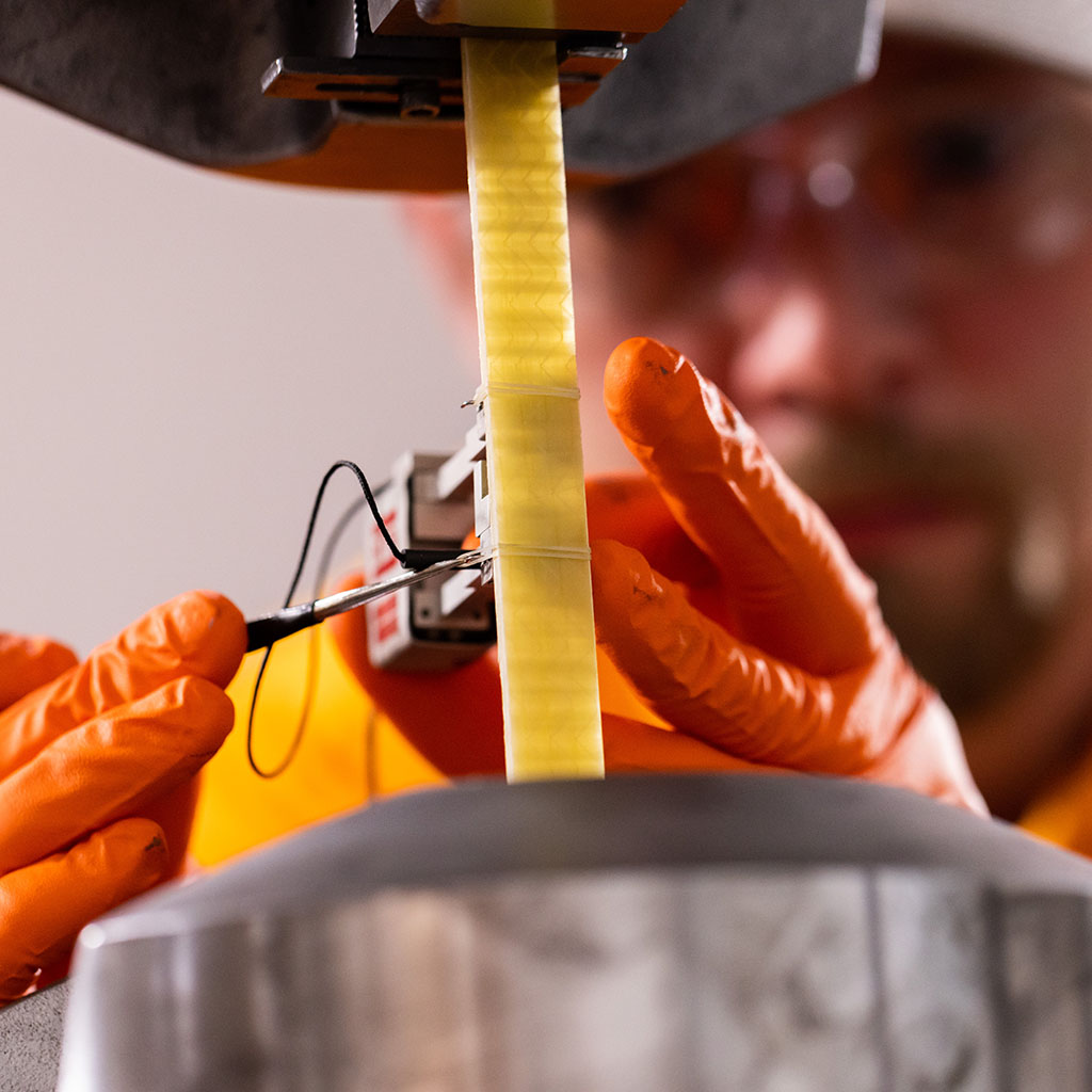 A student wearing orange gloves works on carbon fiber tensile test.