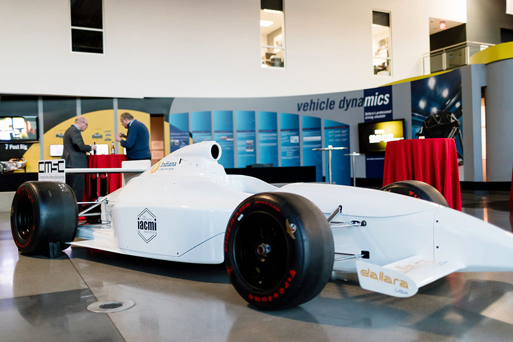 A white Indy race car with the blue IACMI logo in an interior setting.