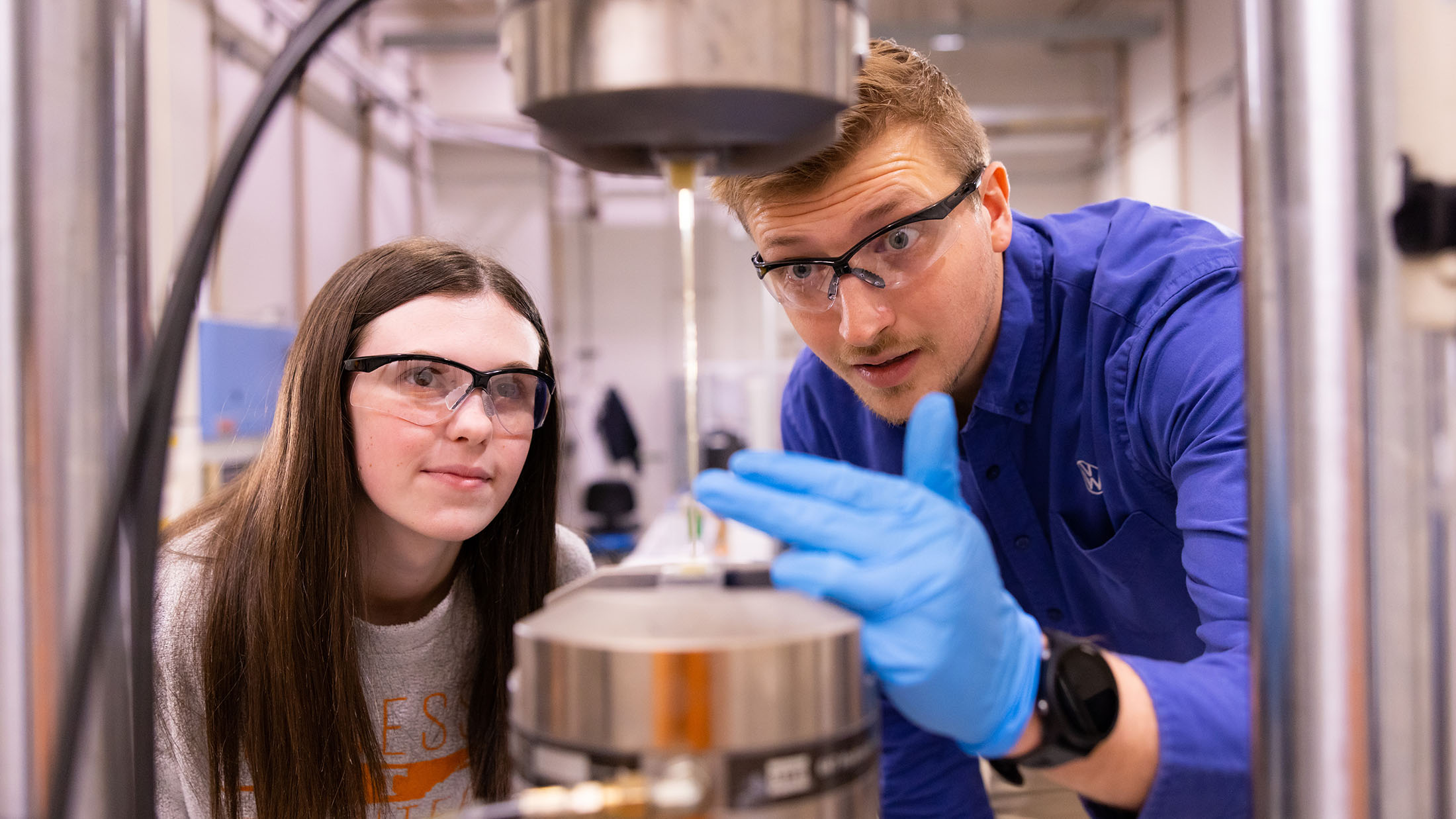 William Henken, a Volkswagen Doctoral Fellow, wears a Volkswagen shirt and helps a female student during a tensile testing of glass fiber reinforced polymeric (GFRP) composites.