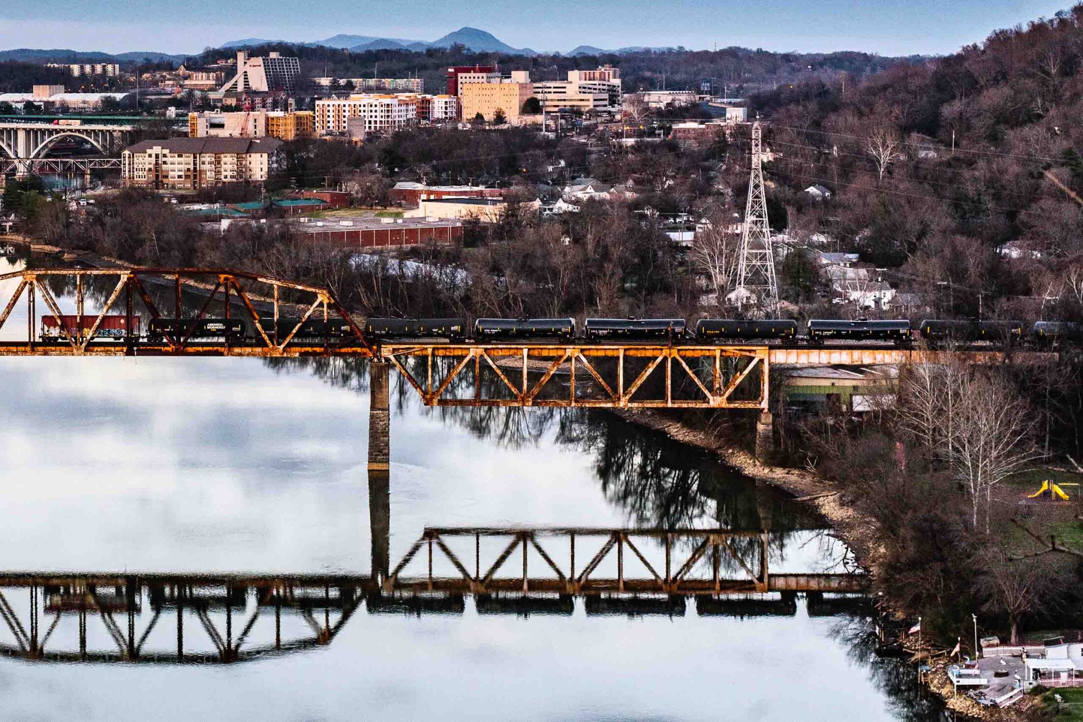 A train crosses the Tennessee River on a bridge with its reflection in the water.