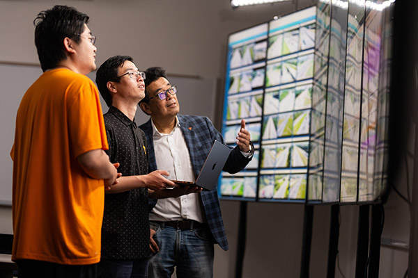 Three men discuss road condition data on a wall of monitors.