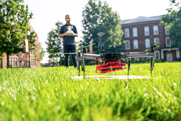 A man flies a drone on the lawn in front of Ayres Hall.