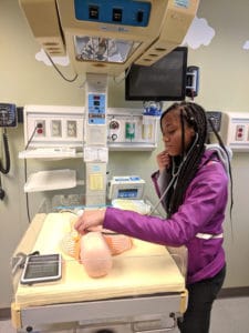 A high school student listens for a heartbeat as she tours lab spaces on Research Day. 