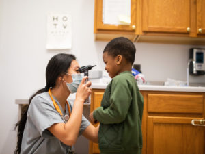 A female nurse inspects the eye of a small boy in a nurse's office.