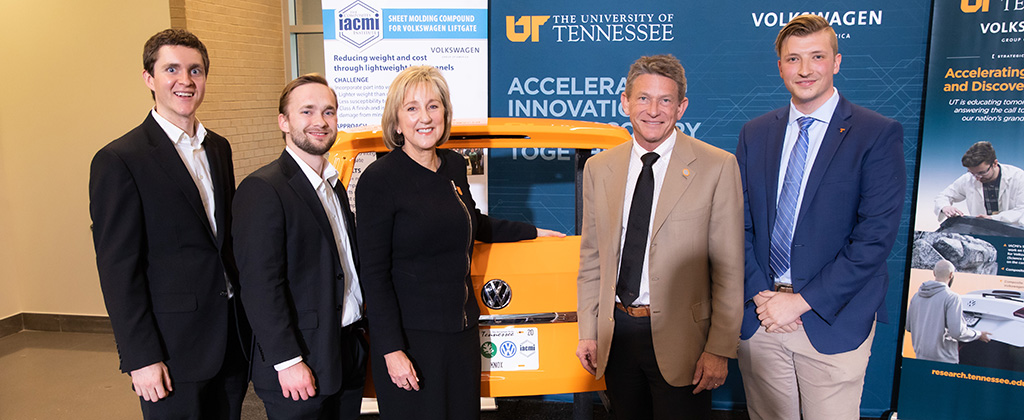 Andrew Foote, Nathan Strain, Chancellor Donde Plowman, President Randy Boyd, and William Henken pose in front of an orange Volkswagen liftgate.