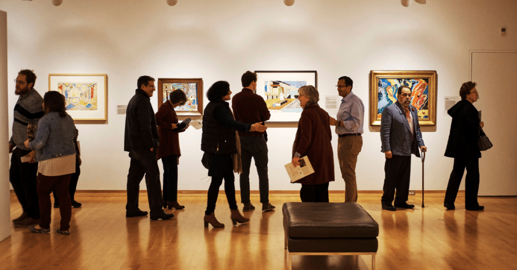 Folks in front of four works of art in a gallery during the Delaney Symposium by the Humanities Center