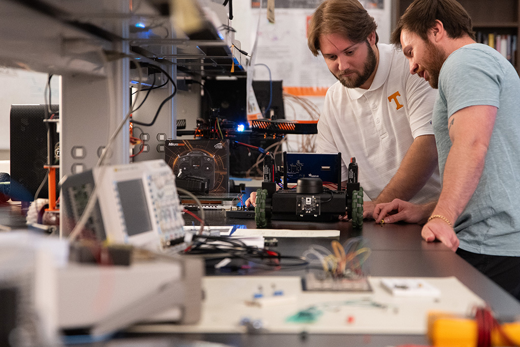 Graduate students Adam Foshie and Charles Rizzo work on an autonomous vehicle in a lab.