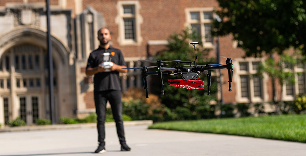 Sabrullah Deniz operates a drone carrying a first-aid package in front of Ayres Hall.