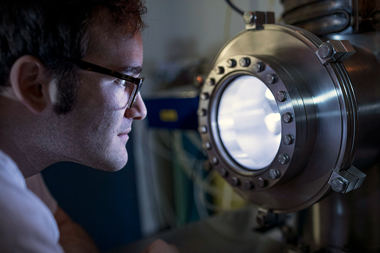 In a dark room, Shawn Zamperini looks into a lighted window of lab equipment.