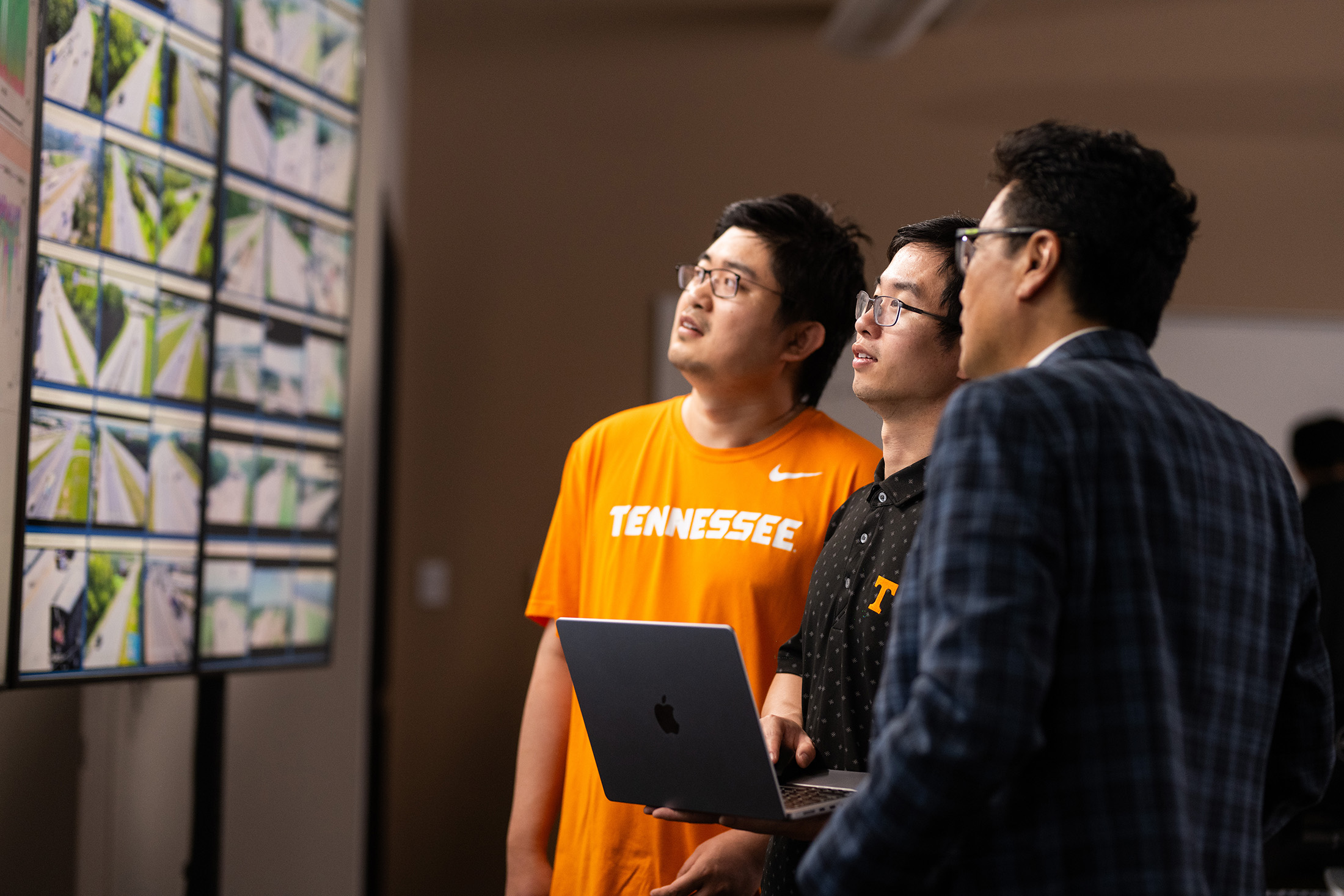Lee Han talks to two graduate students about the content displayed on several monitors with live traffic cams and traffic data.