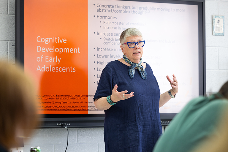 Laurie Meschke speaks in front of a group of teachers in a high school classroom.