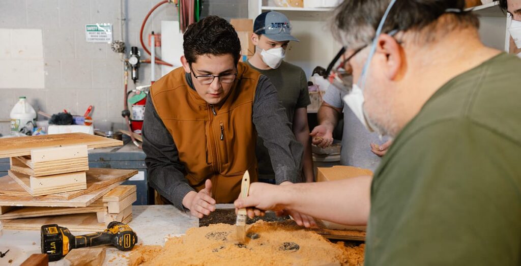 Three participants make sand molds as part of the metal casting portion of METAL Bootcamp at the University of Tennessee, Knoxville's foundry in the Art and Architecture Building.