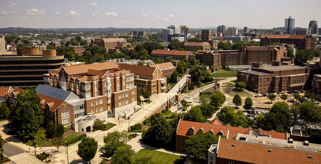 High-angle view of the University of Tennessee campus with brick buildings and the Knoxville Sunsphere in the distance.