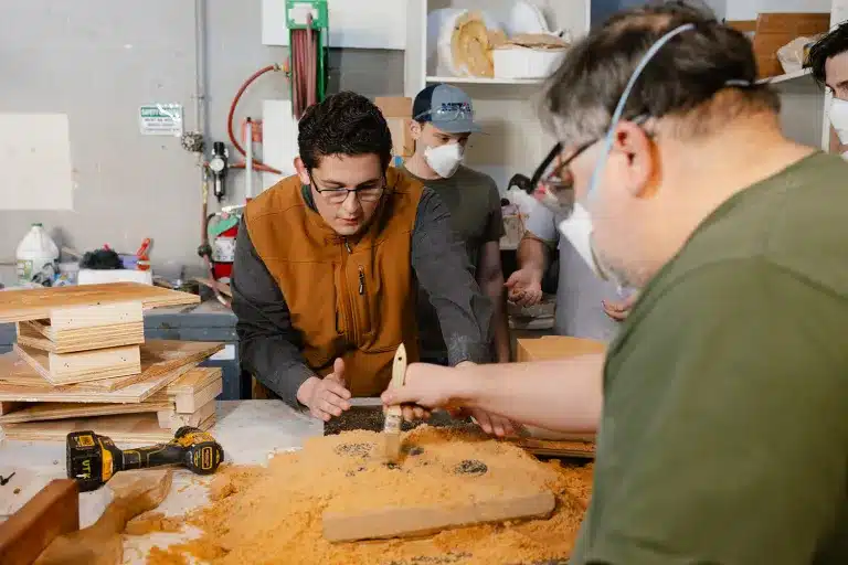 Students and researchers in a workshop preparing a sand casting mold on a workbench.