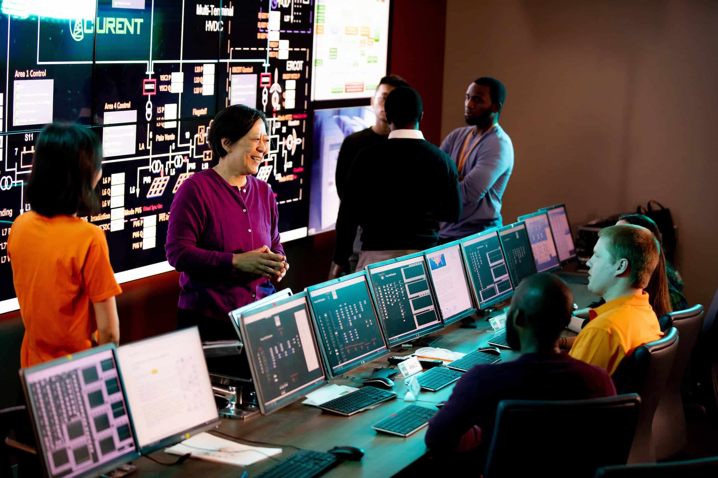 A researcher leading a discussion in a data visualization lab with large screen displays and multiple monitors.