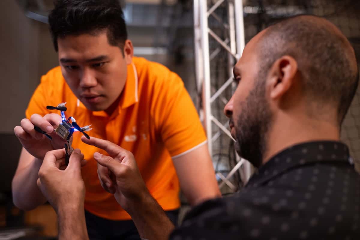 Two researchers collaborating on a small quadcopter drone in a technology lab.