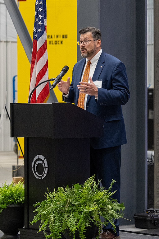 Matthew Mench stands behind a podium on a stage and speaks at the MOU signing event.